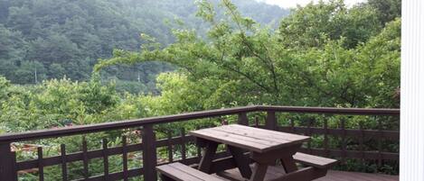 Una terraza de madera con mesas de picnic con vistas a un valle boscoso.
