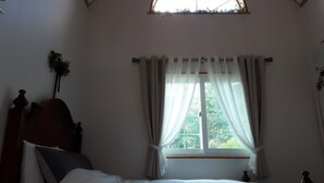 Un dormitorio con cama, cortinas en la ventana, cabecera de madera y una planta pequeña en la pared.