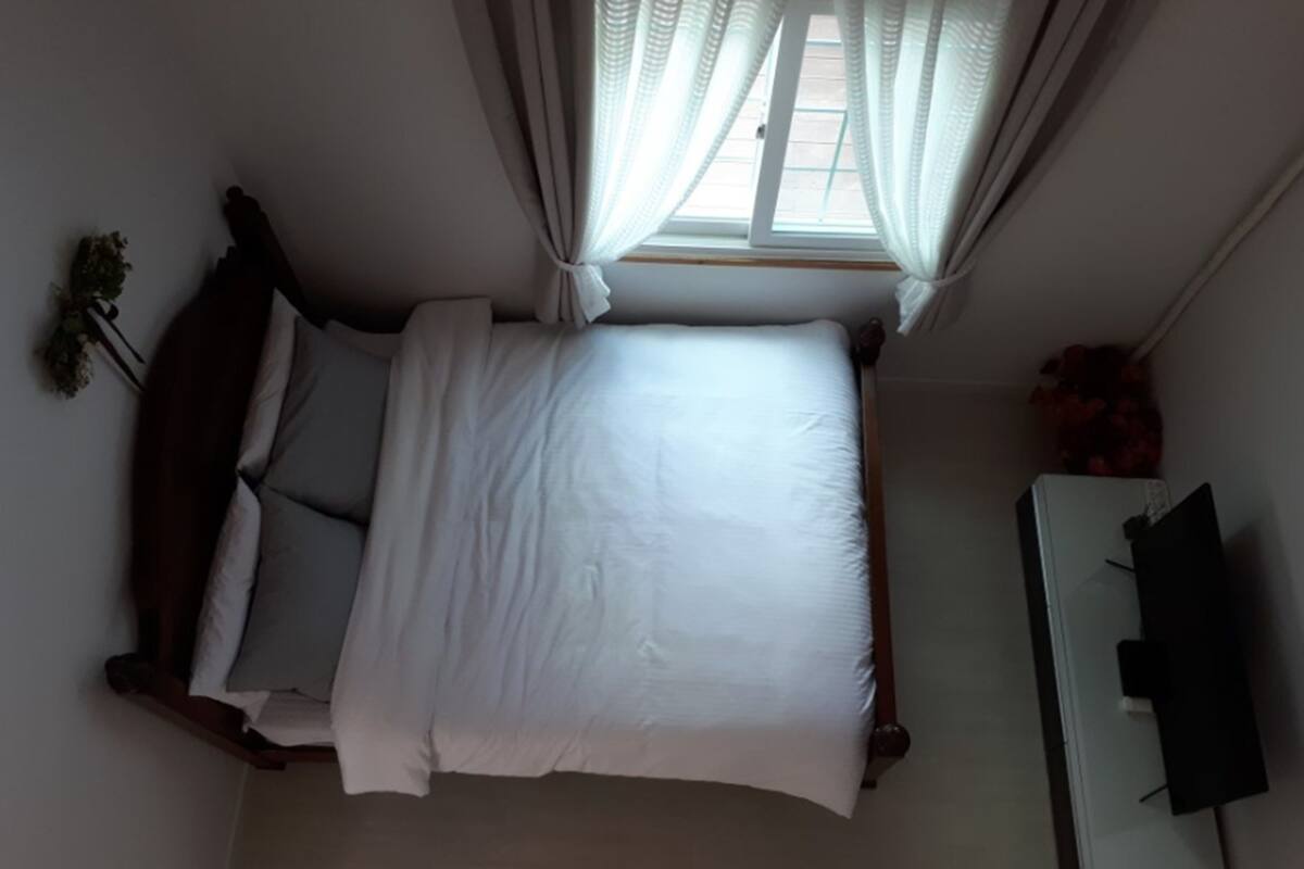 A bedroom with a bed, a TV, and a window with curtains.