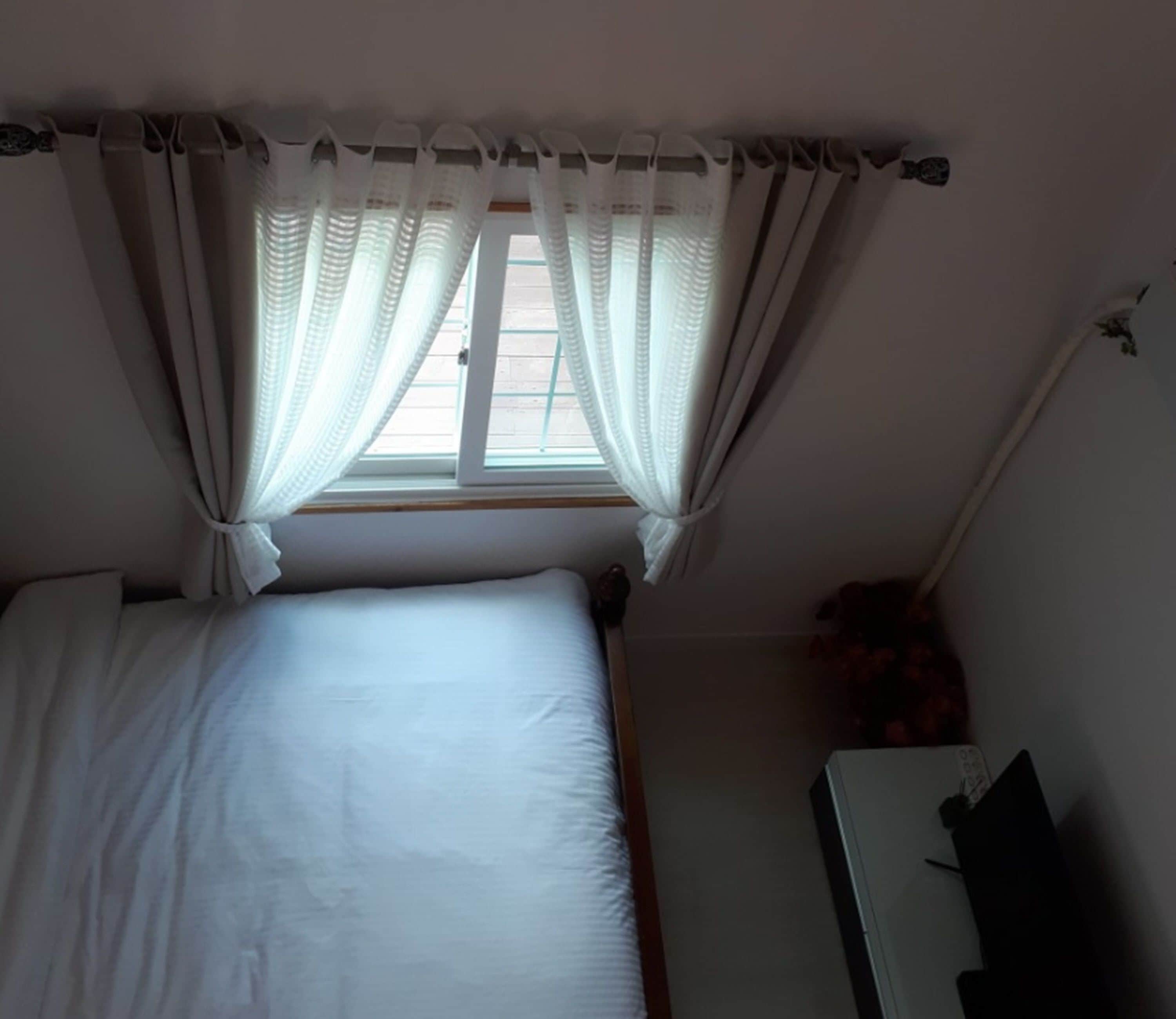 A small, single-bed room with a window and a desk.