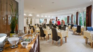 A spacious dining area with multiple tables and chairs, a buffet setup, and large windows offering natural light. - Hotel Nora (Bad Krozingen)