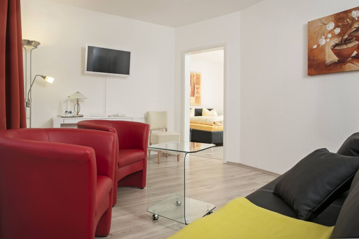 A modern living room with red and black sofas, a glass coffee table, a flat-screen TV, and a painting on the wall.