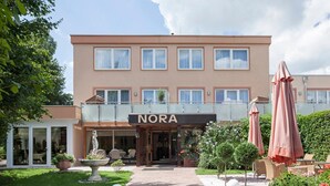 A hotel with a sign reading "NORA" and a covered entrance. There are outdoor seating areas with umbrellas and potted plants. - Hotel Nora (Bad Krozingen)