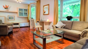 A modern living room with a glass coffee table, a sofa, a chair, and a desk with a lamp. - Hotel Nora (Bad Krozingen)