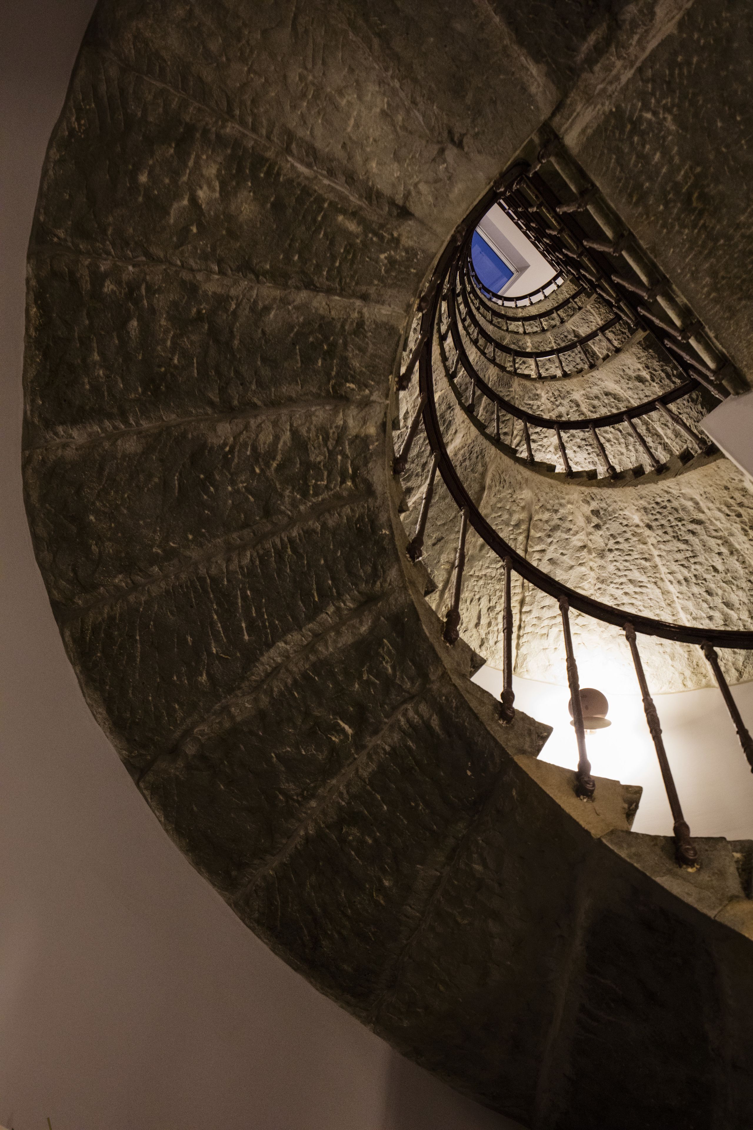 Un escalier en colimaçon avec un mur en pierre et une rampe en métal.