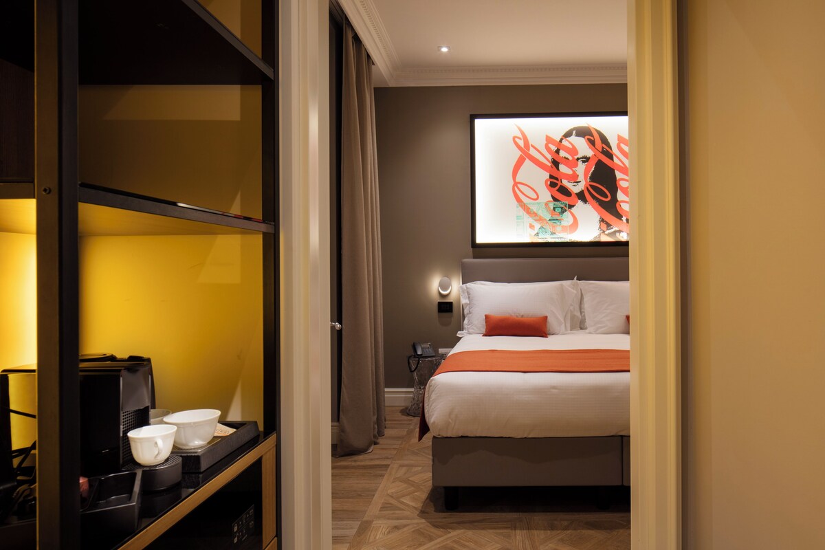 A hotel room with a bed, a coffee machine, and a wall-mounted artwork.