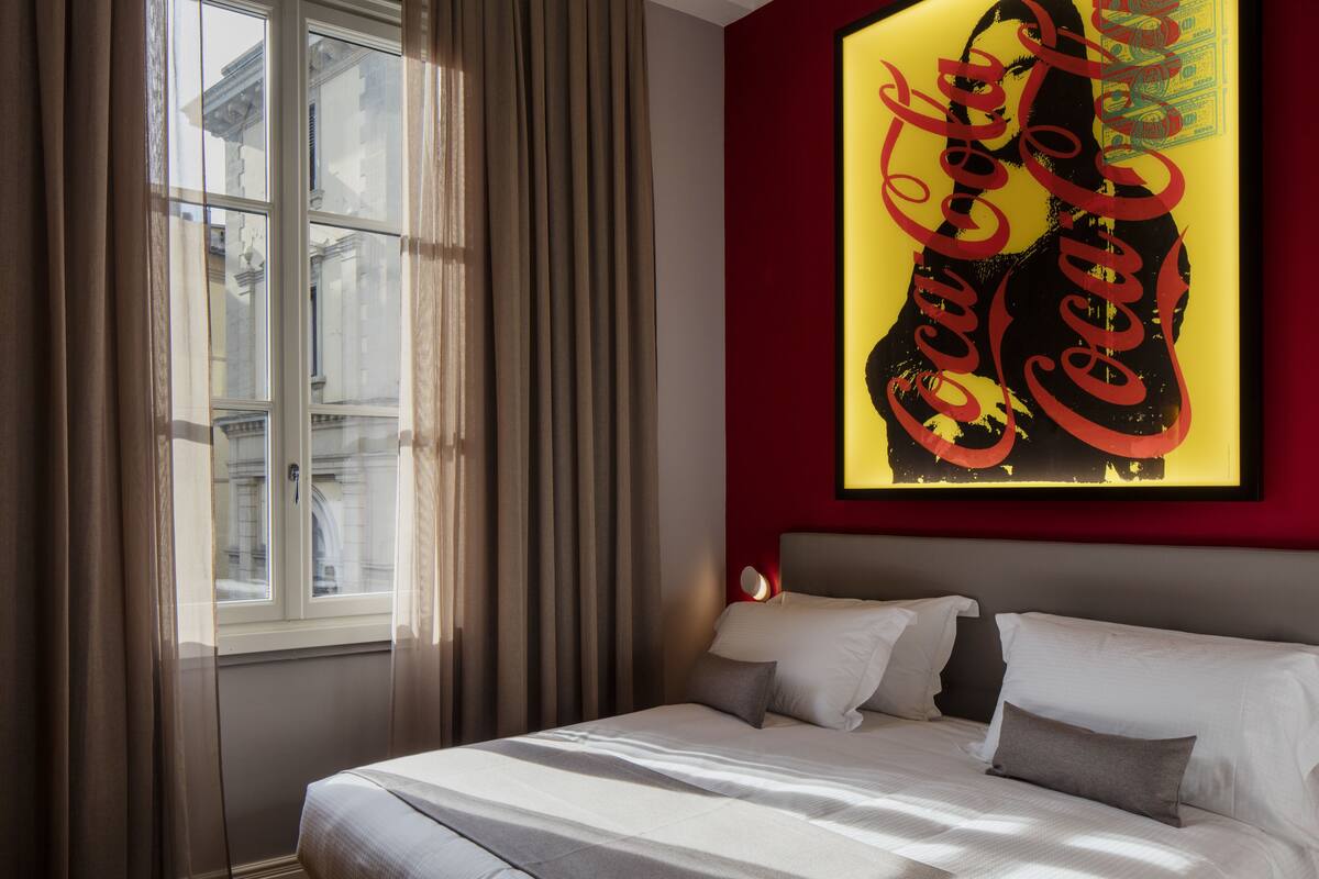 A hotel room with a bed, a window with curtains, and a wall with a Coca-Cola sign.