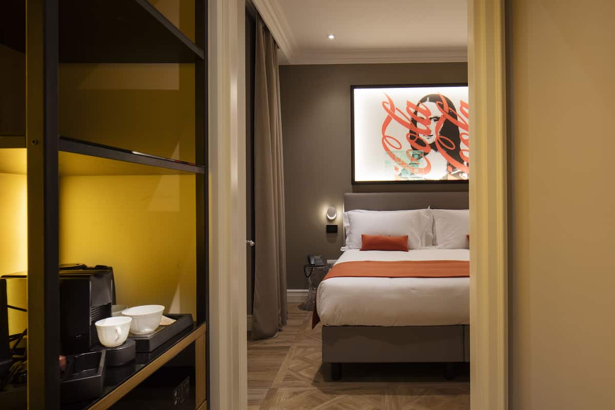 A hotel room with a bed, a coffee machine, and a wall-mounted artwork.