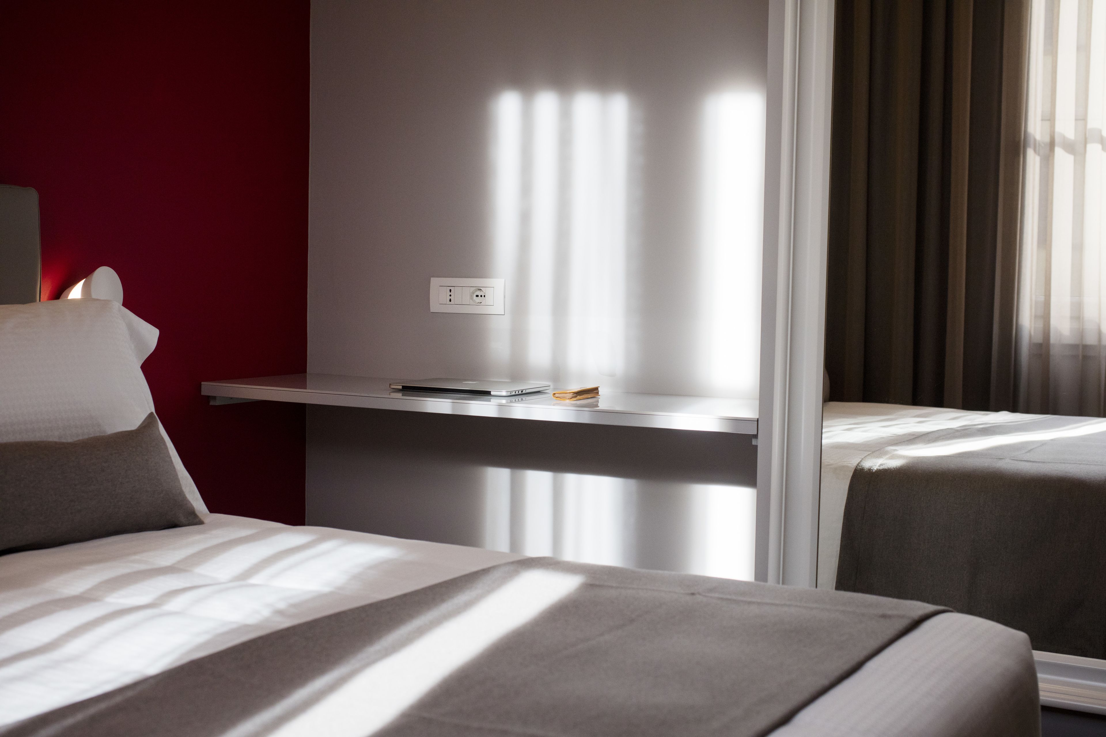 A hotel room with two beds, a desk with a laptop, and a power outlet on the wall.