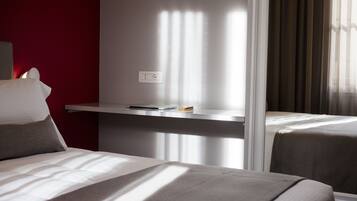 A hotel room with two beds, a desk with a laptop, and a power outlet on the wall.