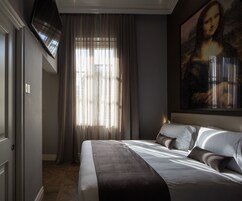 Camera d'albergo con un letto grande, un quadro appeso al muro e una finestra con tende.