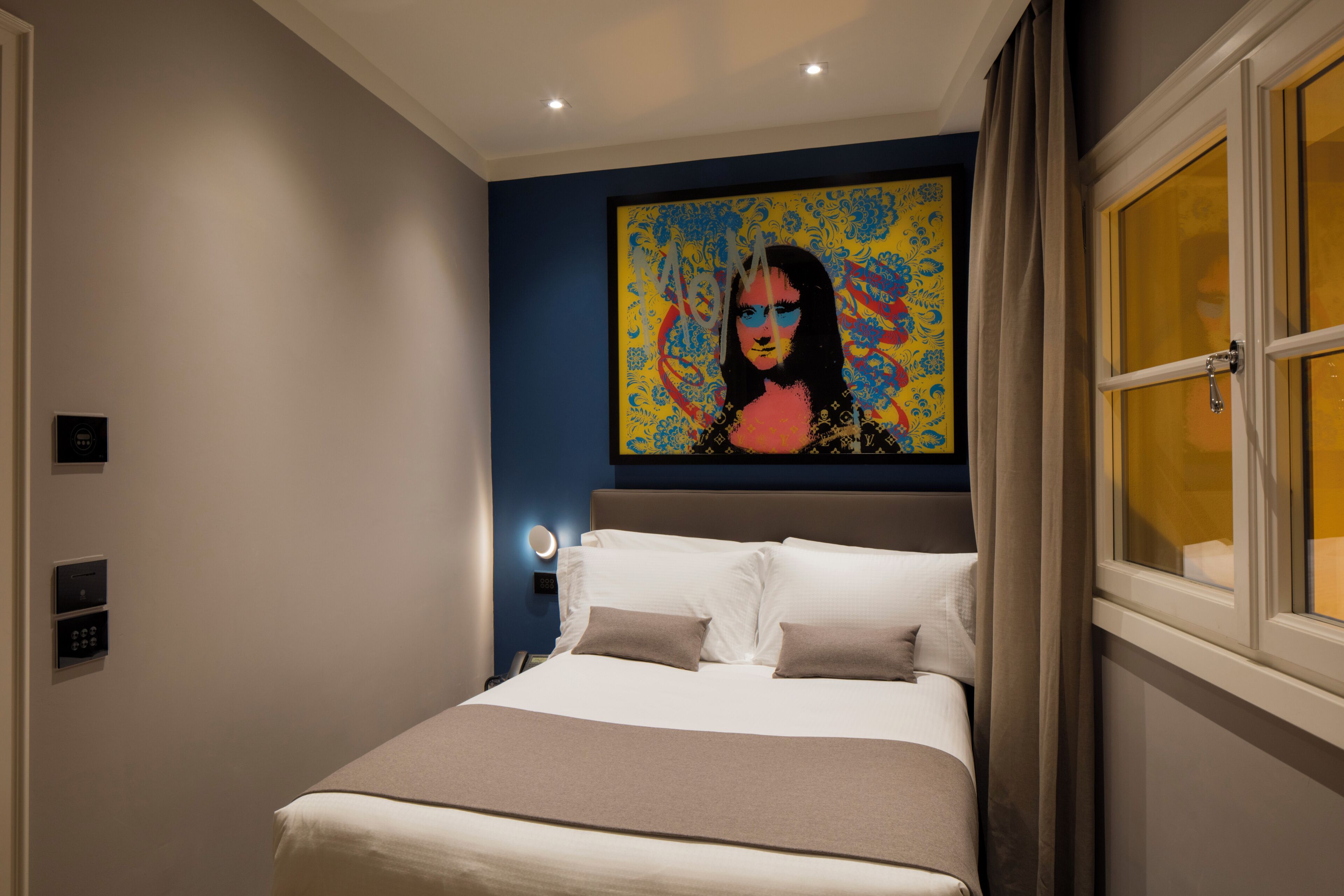 Une chambre d’hôtel moderne avec un grand lit, un tableau accroché au mur et une fenêtre avec des rideaux.