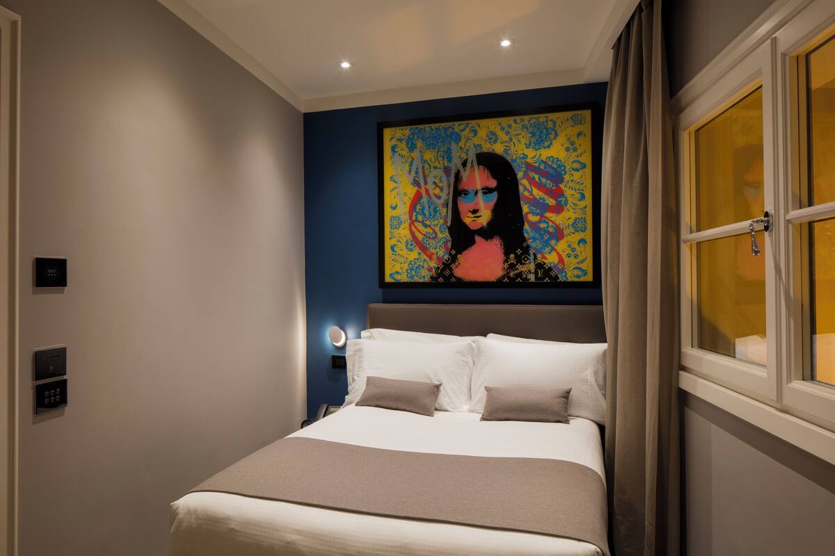 A modern hotel room with a large bed, a painting on the wall, and a window with curtains.
