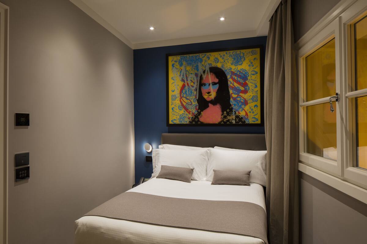 A modern hotel room with a large bed, a painting on the wall, and a window with curtains.