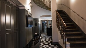 Een moderne hotellobby met een vloer met geometrisch patroon, een statige trap en een receptiebalie.