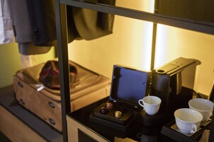 Una camera compatta con una macchina per il caffè, due tazze e una valigia su un tavolo.