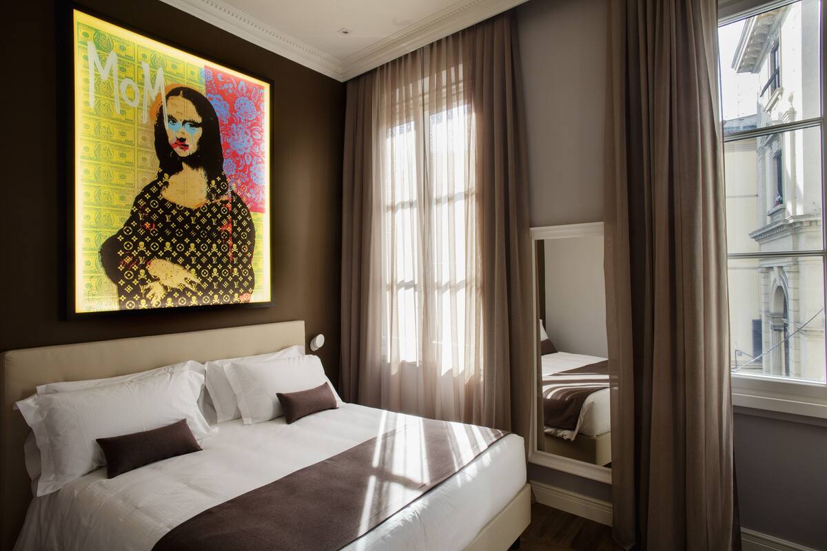 A hotel room with a large bed, a window with curtains, and a wall-mounted artwork.