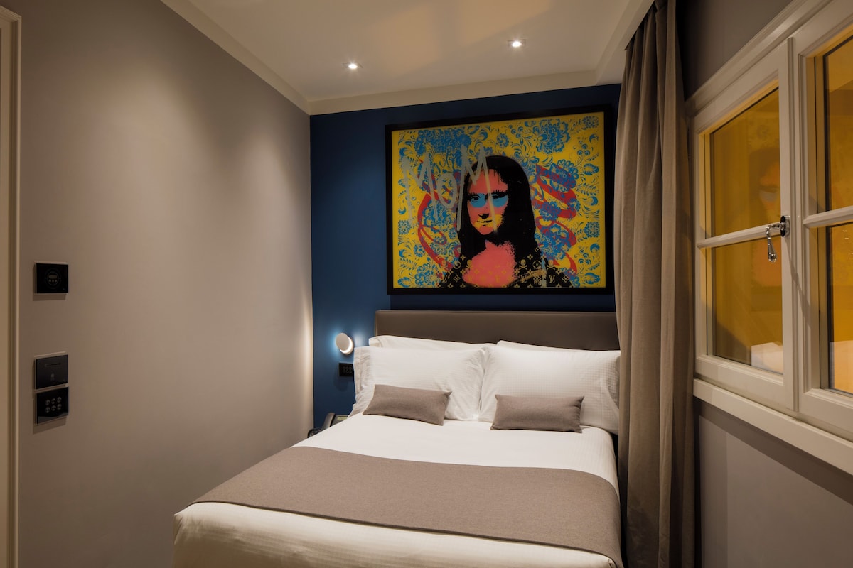 Una habitación de hotel moderna con una cama grande, un cuadro en la pared y una ventana con cortinas.