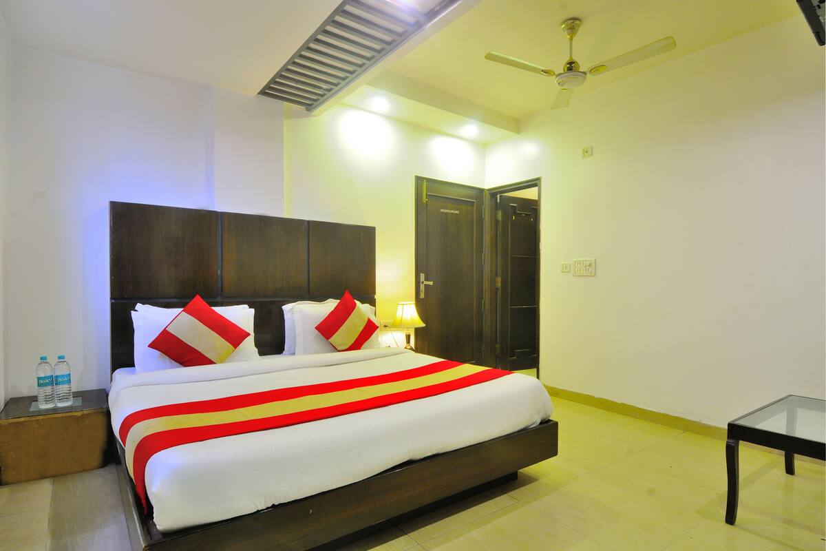 A hotel room with a large bed, a nightstand, a bedside table, a ceiling fan, and a door.