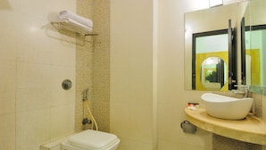 A bathroom with a toilet, a sink with a mirror, and a towel rack. - Hotel Maya Cottage (New Delhi)