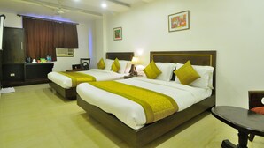 A hotel room with two beds, a desk, a chair, and a table. - Hotel Maya Cottage (New Delhi)