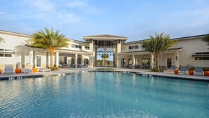 A swimming pool with lounge chairs and palm trees, surrounded by a building with a covered entrance. - Aco238645 - Sonoma Resort - 7 Bed 6.5 Baths Villa (Kissimmee)