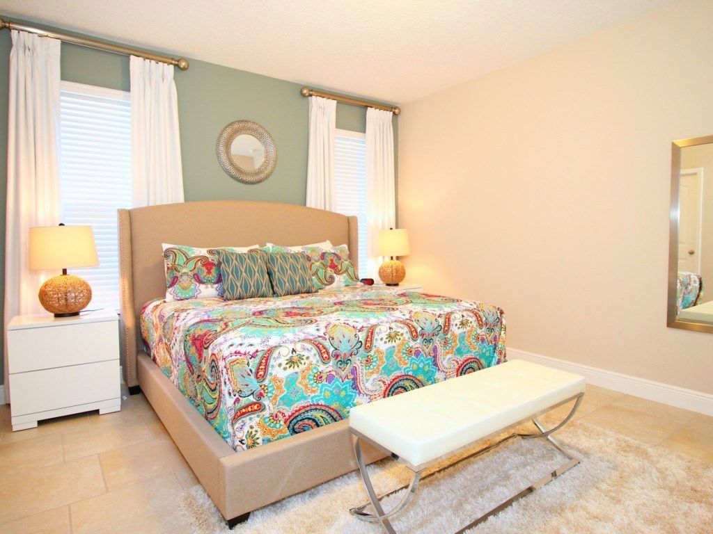 A bedroom with a bed, bedside lamps, a bench, and a mirror on the wall.