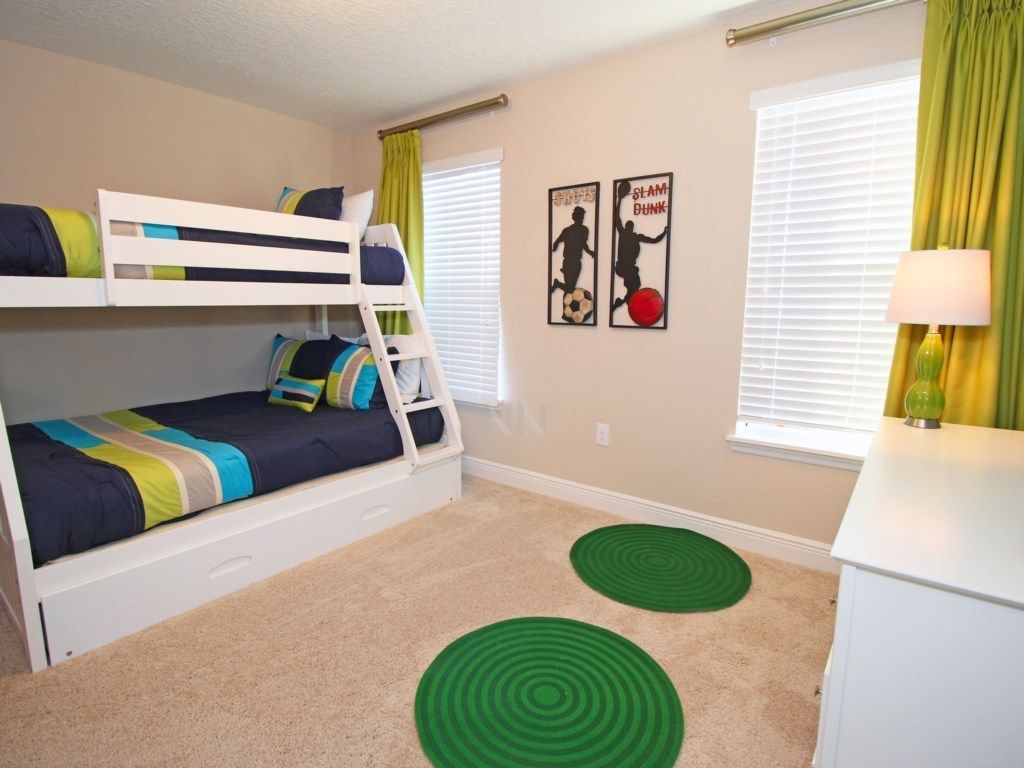 A bunk bed room with two green circular rugs, a desk, and two wall art pieces depicting soccer players.