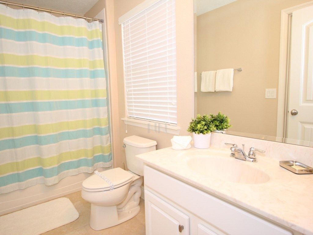 A bathroom with a striped shower curtain, a toilet, a sink with a mirror, and a potted plant.