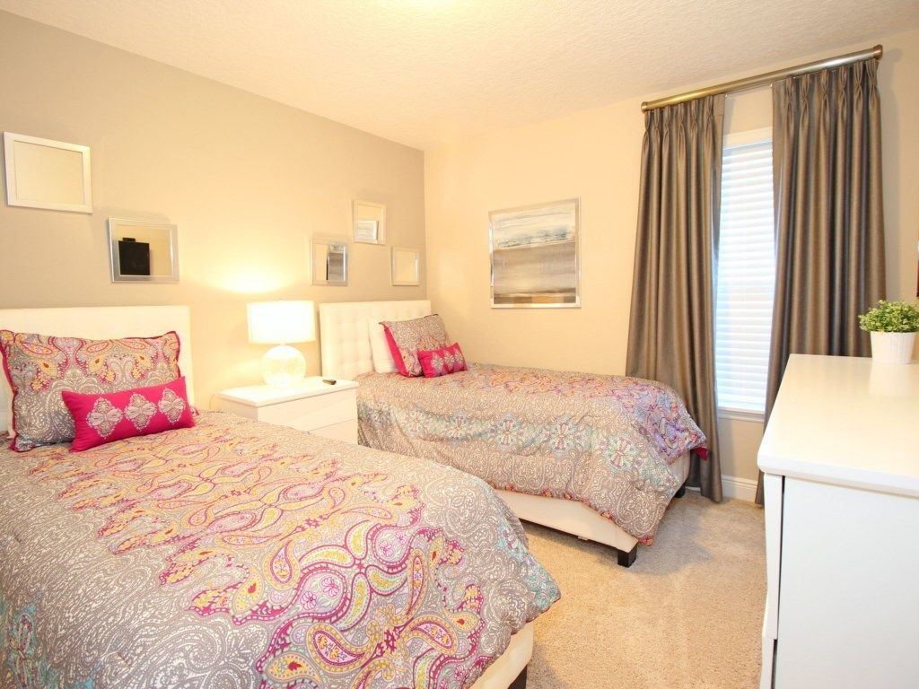 A bedroom with two beds, a bedside table, a lamp, and a window with curtains.