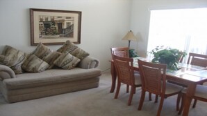 A living room with a beige sofa, patterned cushions, a dining table with chairs, a framed picture on the wall, and a window with natural light. - Ahr104 - Westbury - 4 Bed 3 Baths Villa (Davenport)