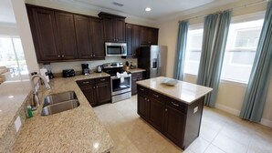 A modern kitchen with dark wood cabinets, stainless steel appliances, granite countertops, and a large island. - Aco231263 - The Encore Club Resort - 6 Bed 6.5 Baths Villa (Kissimmee)