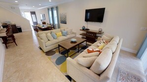 A spacious living room with a beige sofa, a coffee table, and a TV mounted on the wall. - Aco231263 - The Encore Club Resort - 6 Bed 6.5 Baths Villa (Kissimmee)