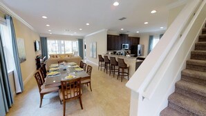 A spacious living area with a dining table set for four, a kitchen with dark cabinets, and a staircase leading to an upper floor. - Aco231263 - The Encore Club Resort - 6 Bed 6.5 Baths Villa (Kissimmee)
