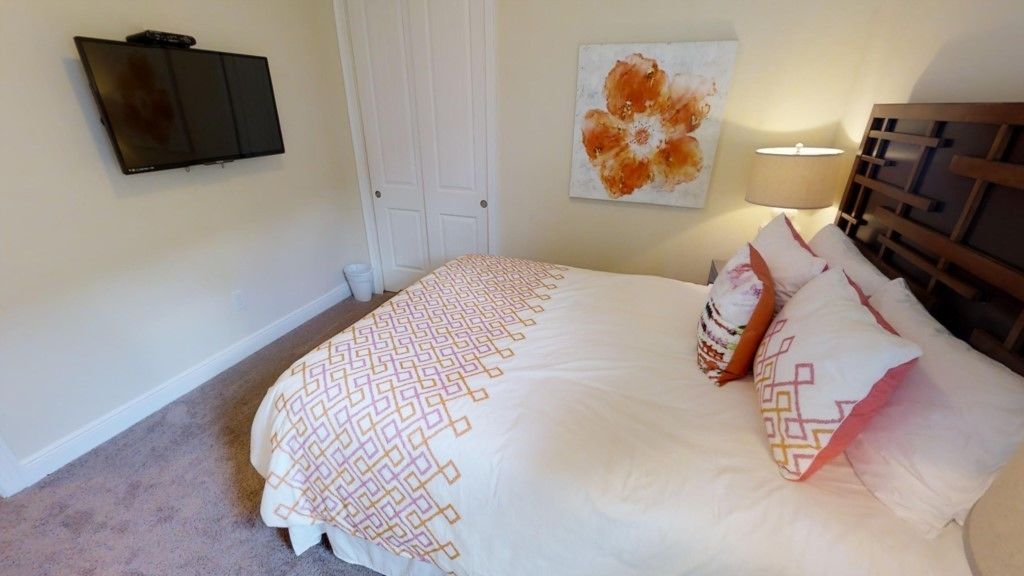 Ein Schlafzimmer mit einem Bett, einem an der Wand befestigten Fernseher, einer Tür und einem Gemälde.