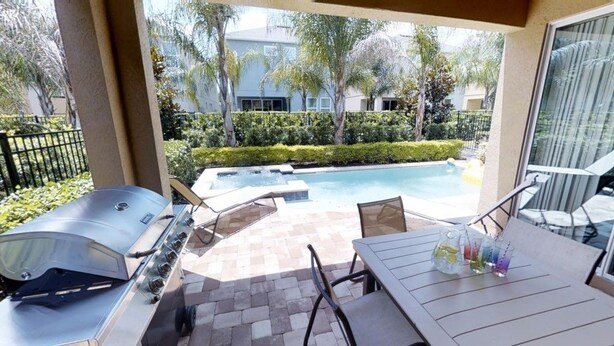 An outdoor patio with a barbecue grill, a table with chairs, and a view of a swimming pool and greenery. - Aco231263 - The Encore Club Resort - 6 Bed 6.5 Baths Villa (Kissimmee)