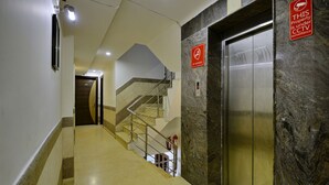 A hotel corridor with a marble wall, a no smoking sign, an elevator, and a staircase. - D Inn (New Delhi)