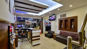 A modern hotel lobby with a reception desk, seating area, and a television displaying travel information. - D Inn (New Delhi)