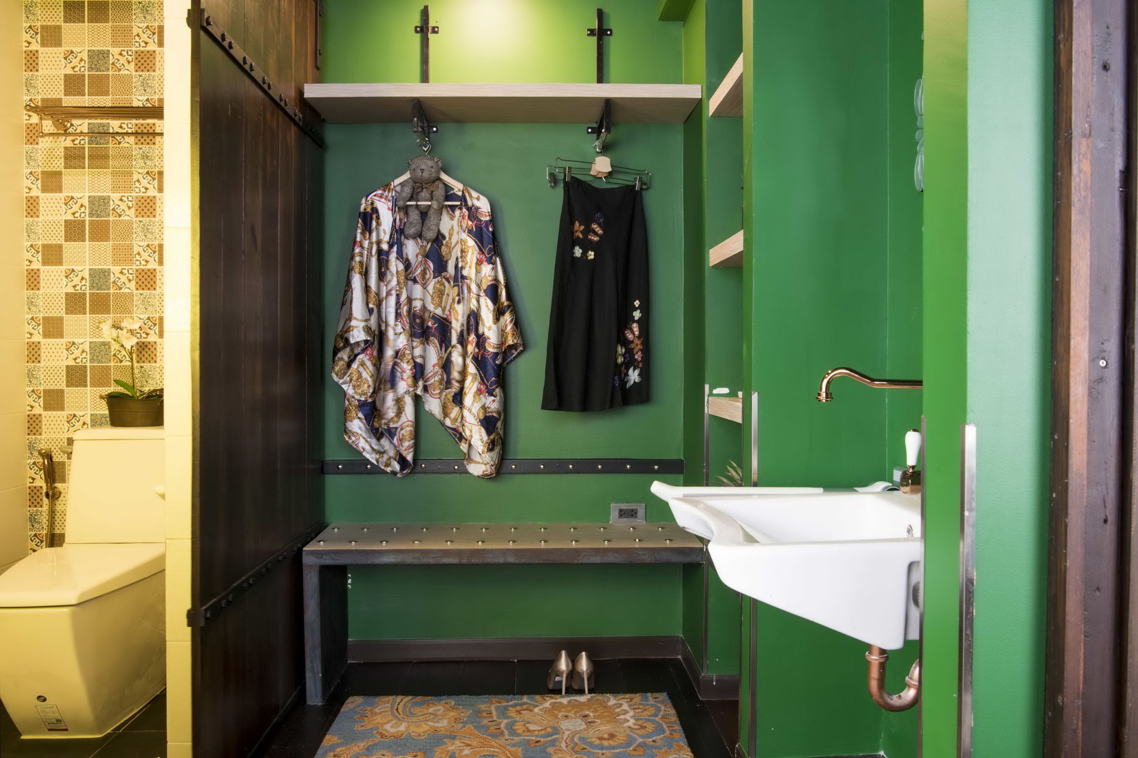 A bathroom with a green wall, a white sink, a bench, and a hanging rack with clothes and a teddy bear.