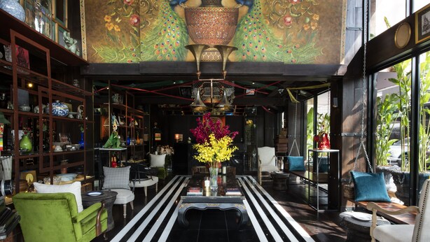 Un vestíbulo de hotel con piso a rayas blanco y negro, un arreglo floral central y un mural de pavo real en el techo.
