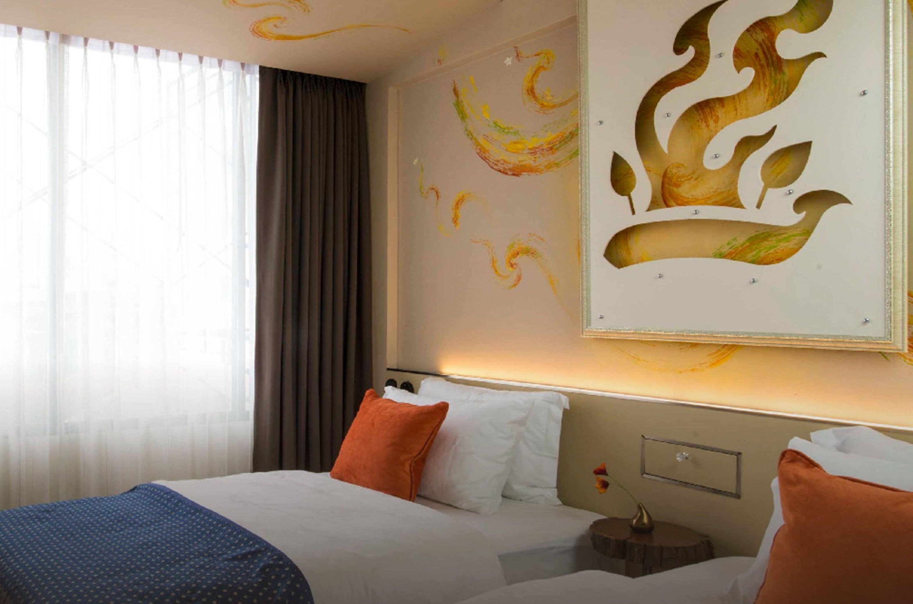 Habitació d'hotel amb un llit gran, dos coixins, una tauleta de nit i un mural a la paret.