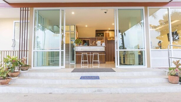 Une entrée d’hôtel moderne avec des portes vitrées, un petit espace extérieur aménagé avec des sièges et des plantes en pot.