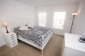 A bedroom with a zebra-patterned bedspread, a white metal headboard, a bedside table with a lamp, and a desk with a hairdryer. - Ip60172 - Club Cortile Resort - 3 Bed 2 Baths Condo (Kissimmee)