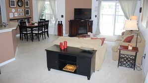 Ein Wohnzimmer mit einer Couch, einem Couchtisch, einem Fernseher und einem Essbereich mit Stühlen und einem Tisch.