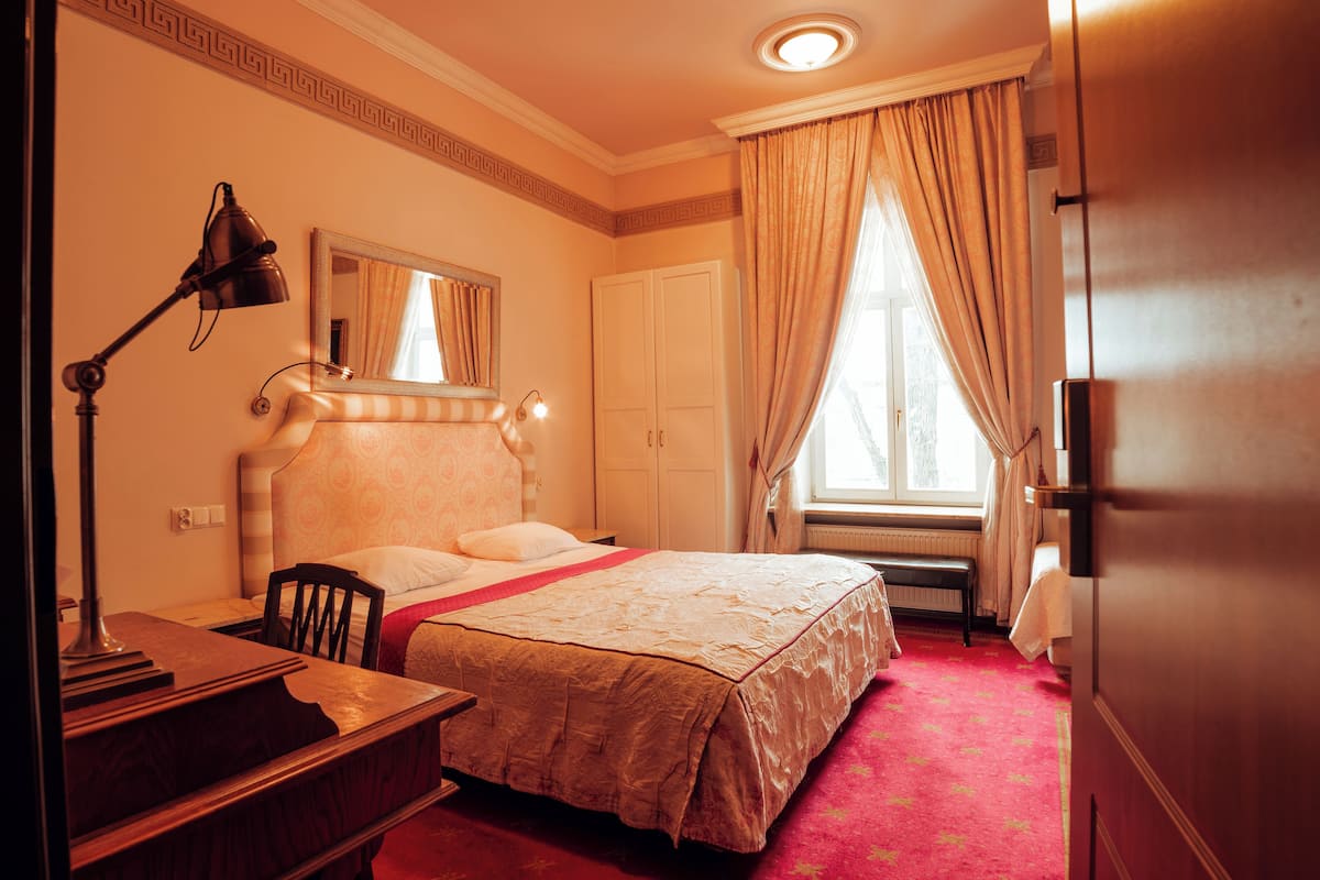 Une chambre d’hôtel équipée d’un lit, d’un bureau, d’une chaise, d’une lampe et d’une fenêtre avec des rideaux.