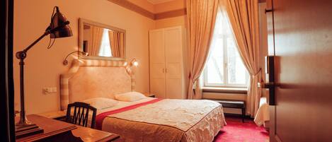 A hotel room with a bed, desk, chair, lamp, and a window with curtains.
