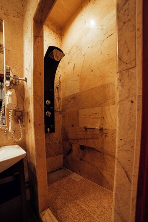 A bathroom with a marble wall, a shower, and a sink with a telephone.