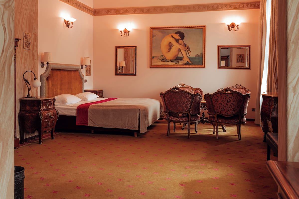 Une chambre d’hôtel avec un lit, deux chaises, une commode et un tableau au mur.