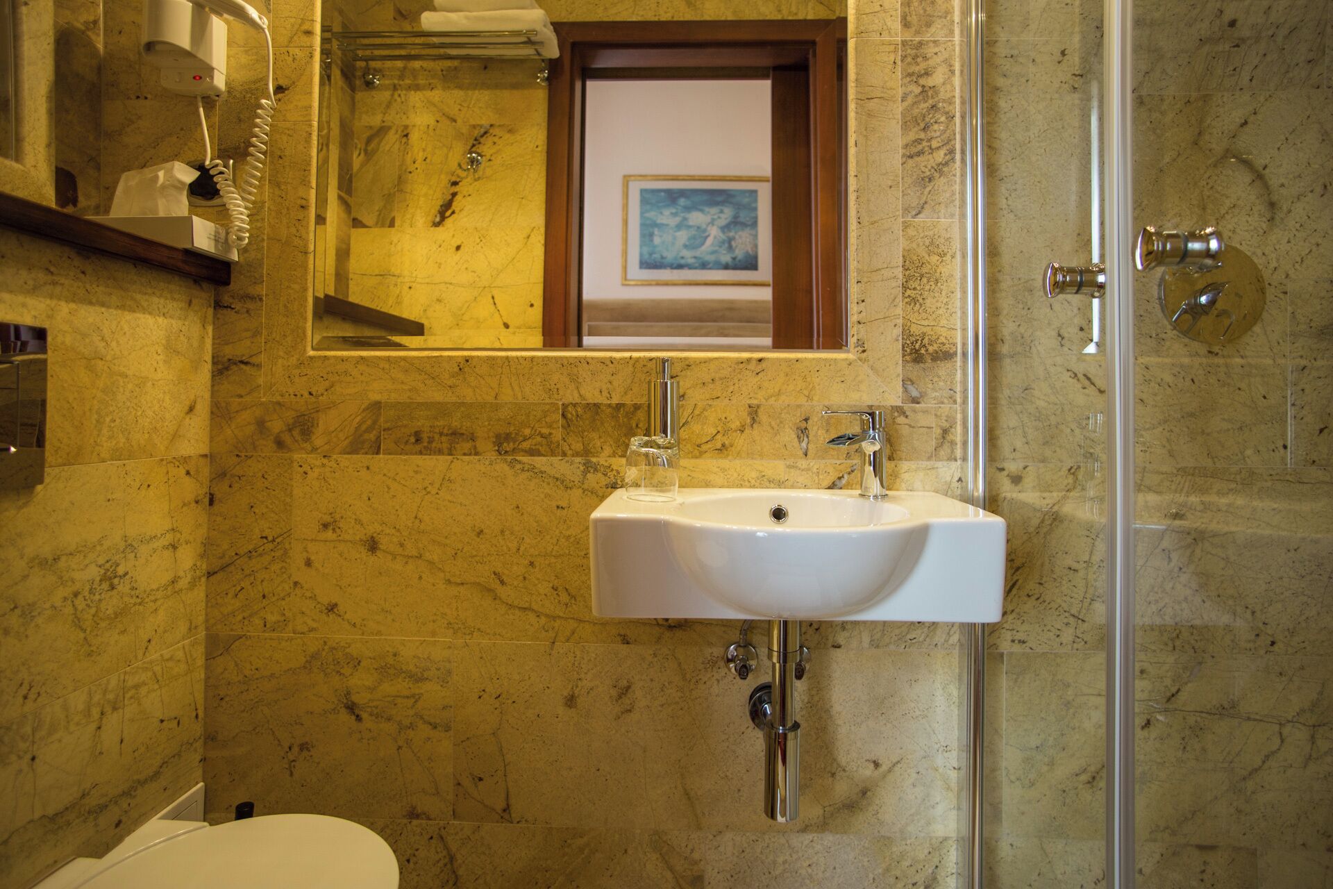 A bathroom with a white sink, a glass shower enclosure, and a marble-tiled wall.