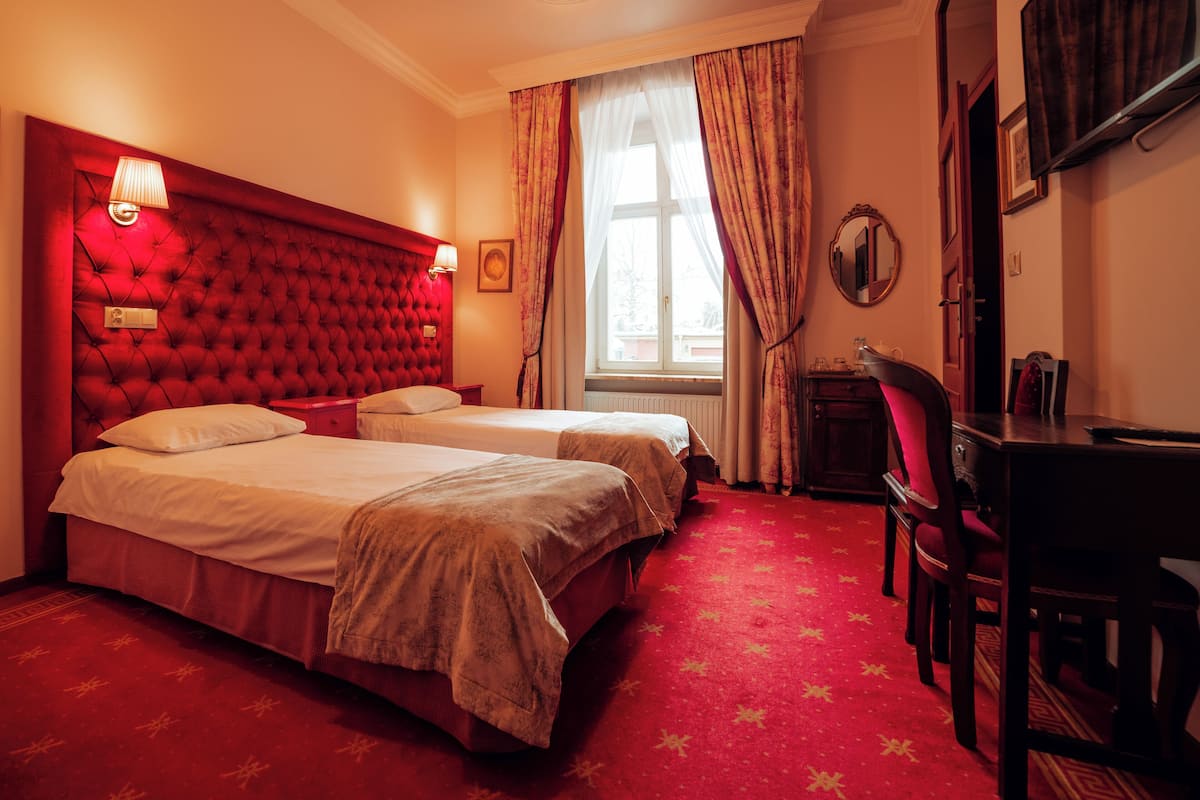 Une chambre d’hôtel avec deux lits, une tête de lit rouge recouverte de tissu et un bureau avec une chaise.